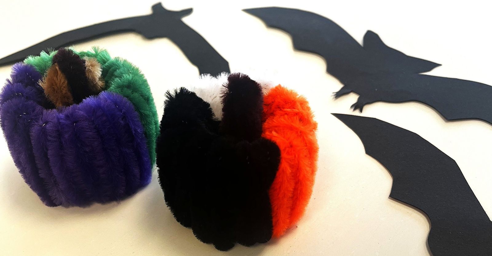 Halloweenpyssel med piprensare – två små färgglada pumpor och svarta pappersfladdermöss som dekoration.